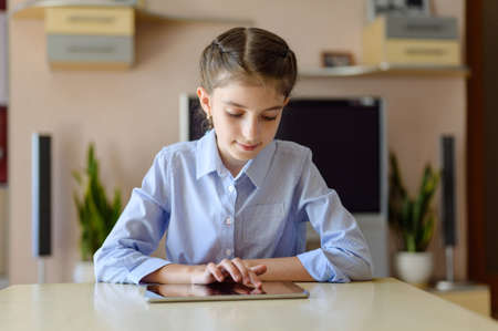 girl sitting in a room at a table with a tablet. A girl moves her finger on the touch screen.の写真素材