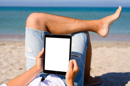 A man is resting on the beach with a tablet. Close-up. Free space for text.の写真素材