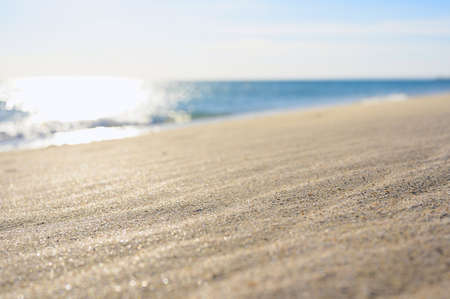 Sandy beach in windy weather. In the background the sea and the sun. Focus on the sand, blurred...