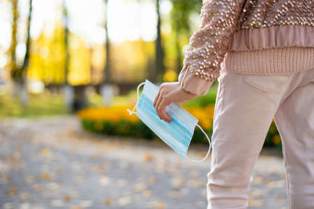 Medical mask in the hand of a teenage girl on a walk. The concept of using protective equipment during quarantineの写真素材
