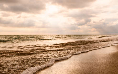 Seascape in the evening. Sun rays shine through the clouds. Focuses on the water's edge and sand.の写真素材