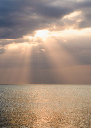 Sunset over the sea. The sun's rays shine from behind the clouds. Vertical frame.の写真素材