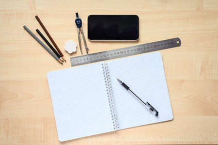 Items for an online lesson on the table. View from above. Notebook with blank pages, ruler, pencils, pen, compasses and telephone on the desk. Training concept during quarantine.の写真素材