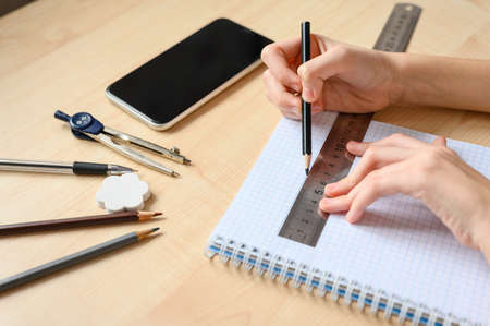 The student does his homework and draws a line with a ruler. Shooting close-up. Focus on pencil and ruler. Home learning concept.の写真素材