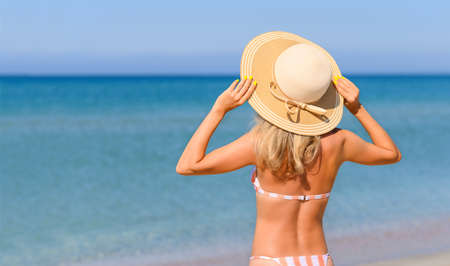 A slender girl in a straw hat stands on the seashore on a sunny day. Beach vacation in a tropical climate.の写真素材