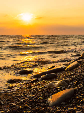 Sunset at the sea. Vertical frame. Pebble beach and surf at sunset. Focusing on tracing pebbles in the foreground.の写真素材