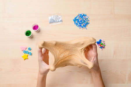Slime toy in the hands of a child. In the background there is a table and ingredients for decorating the slime. Focusing on the slime.の写真素材