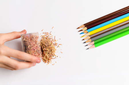 A child's hand pours the shavings from the pencils onto the white paper. Colored pencils lie nearby.の写真素材