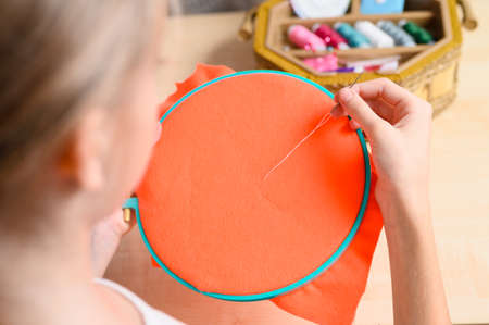 The girl is learning to embroider. The girl is holding a hoop with an orange cloth and a thread with a needle. Focusing on the hand with a needle.の写真素材