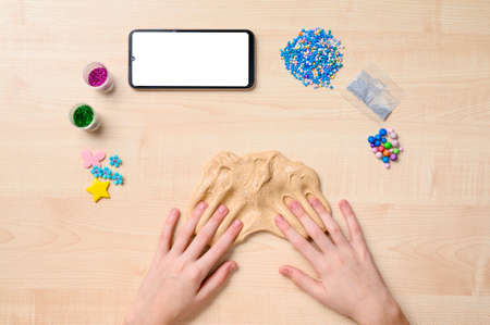 Making slime using the Internet. Children's hands on the table and slime. Next to a smartphone with a blank white display.の写真素材
