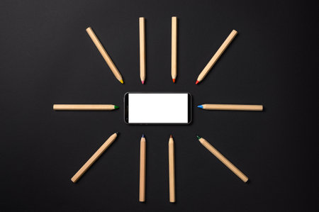 Pencils lie around the smartphone on a black background. Smartphone with blank white displayの写真素材