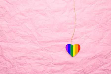 Lgbt heart on a string on a crumpled pink background. Lgbt relationship concept. There is a free space on the leftの写真素材