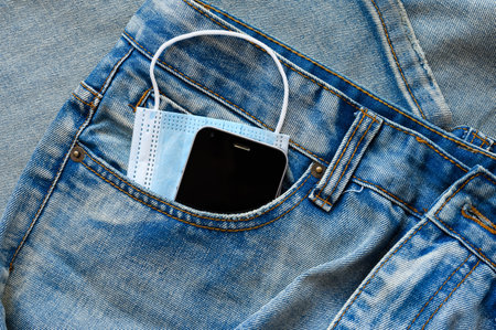Blue medical mask and black smartphone in the pocket of blue jeans.の写真素材