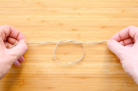 Human hands tie a knot on a rope on a wooden background. The concept of friendship and love charms.の写真素材
