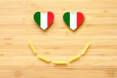 Pasta smile and heart-shaped eyes in the color of the flag of Italy on a wooden background. Concept of love of Italy and Italian pasta.の写真素材