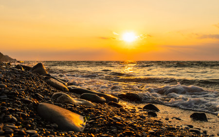 Rocky seashore against the sunset. A golden sunset on the seashore and a foaming sea. Focusing on the water's edge.の写真素材