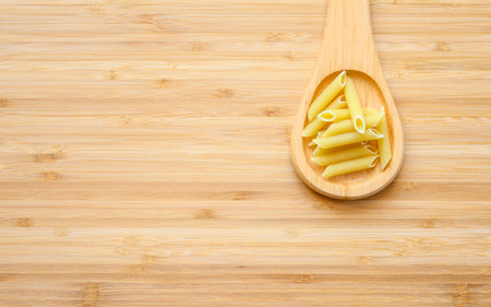 A wooden spoon with pasta lies on a wooden board. There is an empty space to the left of the spoon for text. The concept of a recipe for making pasta.の写真素材