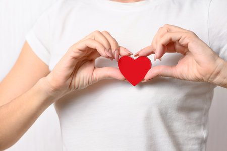 The girl holds a red heart on her chest as a symbol of love and health. Heart disease conceptの写真素材