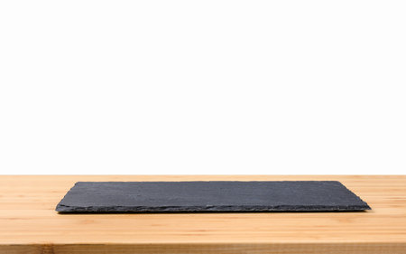 Black dish made of natural stone on a wooden table. at the table empty white isolated background. Rectangular black slate plate. Focusing on the center of the cymbalの写真素材