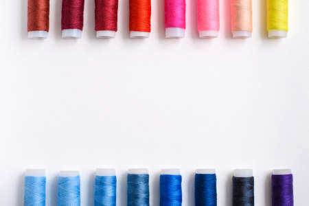 Multi-colored spools of thread arranged evenly along the edges on a white background. There is an empty space in the center of the frame.の写真素材