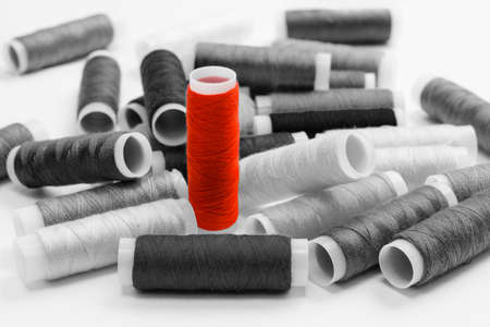 Lots of scattered black and white spools of thread and one red one. One spool of thread stands out from the others. Leadership and creative thinking concept.の写真素材