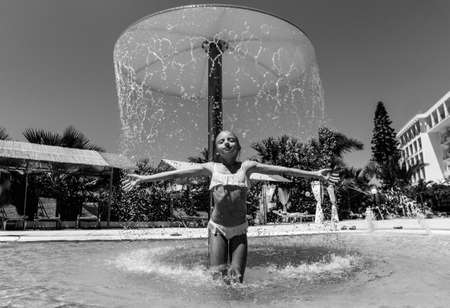 A girl in a pool on a sunny day under streams of water. Black and white portrait of a girl on a hot day by the poolの写真素材