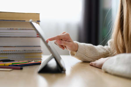 The girl at home uses a tablet for homework or searching the Internet. close-up. Selective focus on the hand.の写真素材
