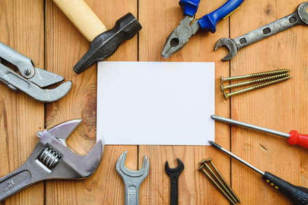 Repair and construction tools lie on a wooden table around a white blank sheet. Construction and renovation work concept.の写真素材
