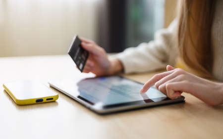 The girl makes a payment with a bank card on the Internet on a tablet. Close-up. Selective focus on the hand near the tablet display.の写真素材