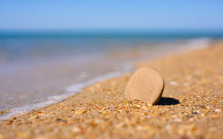 A flat small stone stands on the seashore. Place for text on the stone. In the background the sea. Blank for an inscription on the theme of sea recreation.の写真素材