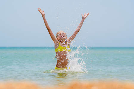 Joyful girl in the sea splashes water. A lot of water spray around the girl.の写真素材