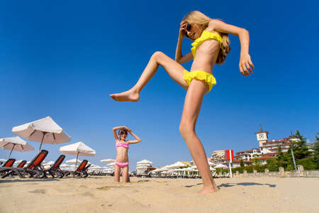 Two girls play and have fun on the beach. One big girl holds her foot over a little girl.の写真素材