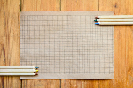 Old sheet of paper with pencils on a wooden surface. Free white space on the sheet for text or sketchの写真素材