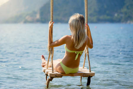 Girl resting on a swing in the seaの写真素材