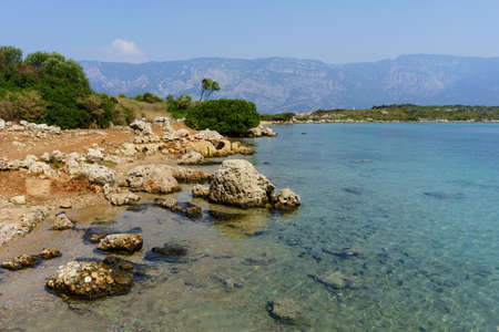 The shore of the island in the Aegean against the backdrop of the mountains. Big stones lie in the waterの写真素材