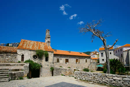 Old building in the old part of Budva. White cloud over a dry tree.