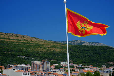 Montenegro flag is developing in the wind against the background of the spa town of Petrovacの写真素材