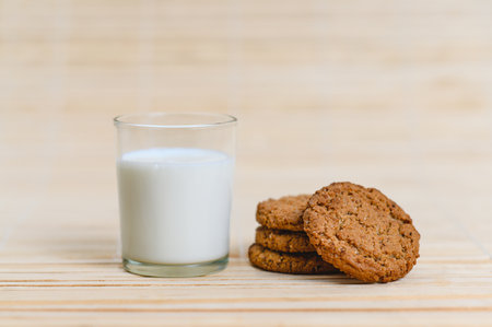 a glass of milk is next to a homemade oatmeal cookie on a wooden surface.の写真素材