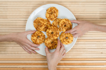 Three hands reach for fresh homemade cookies. A lot of cookies lie on a big white plateの写真素材