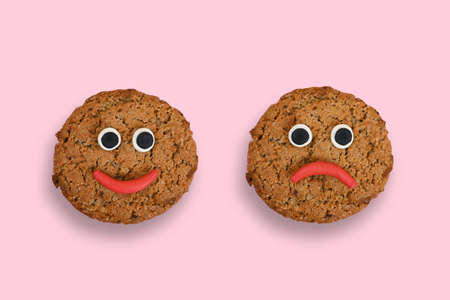 Two oatmeal cookies in the form of emoticons on a pink background. One smiley is smiling, the other is sad.の写真素材