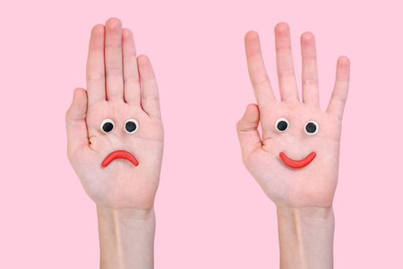 Two hands on a pink background with plasticine eyes and lips.の写真素材