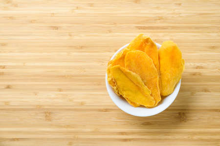 Healthy and healthy breakfast concept. Dried mango slices in a white bowl on a wooden table. Free empty space on the leftの写真素材