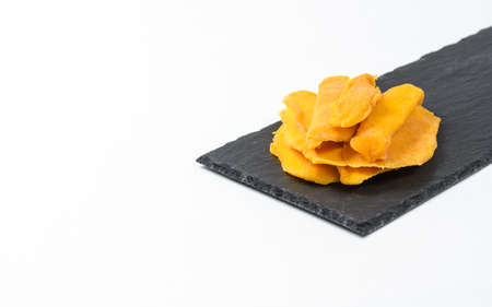 Dried mango slices lie on a black slate plate on a white plate. Isolated object. There is a free empty space on the left. Healthy food concept.の写真素材