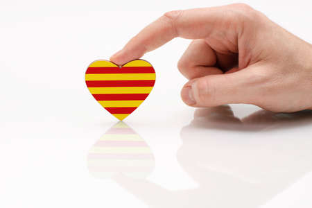 Flag of Catalonia. Love and respect Catalonia. A man's hand holds a heart in the shape of the Catalunya flag on a white glass surface. The concept of patriotism and pride.の写真素材