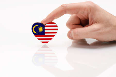 Love and respect Malaysia. A man's hand holds a heart in the shape of the Malaysia flag on a white glass surface. The concept of Malaysian patriotism and pride.の写真素材