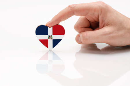 Dominican Republic flag. Love and respect to the Dominican Republic. A man's hand holds a heart in the shape of the Dominican Republic flag on a white glass surface. The concept of patriotism and pride.の写真素材