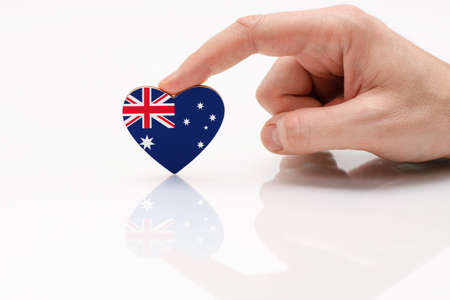 Love and respect Australia. A man's hand holds a heart in the shape of the Australia flag on a white glass surface. The concept of Australian patriotism and pride.の写真素材