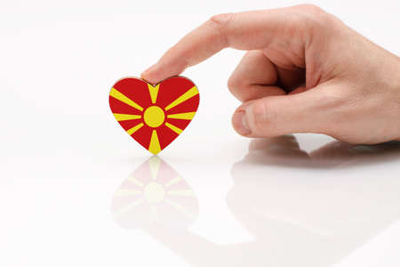 Flag of Macedonia. Love and respect Macedonia. A man's hand holds a heart in the shape of the Macedonian flag on a white glass surface. The concept of Macedonian patriotism and pride.の写真素材