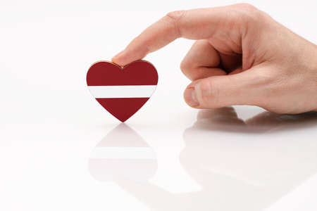 Love and respect Latvia. A man's hand holds a heart in the shape of the Latvian flag on a white glass surface. The concept of Latvian patriotism and pride.の写真素材