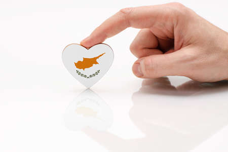 Cyprus flag. Love and respect Cyprus. A man's hand holds a heart in the shape of the Cyprus flag on a white glass surface. The concept of Cypriot patriotism and pride.の写真素材